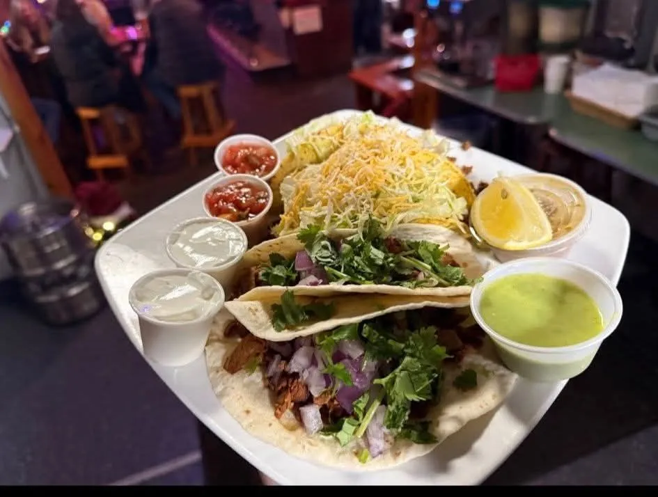 Street-style carnitas tacos with cilantro and red onion, held up against the warmly lit bar.