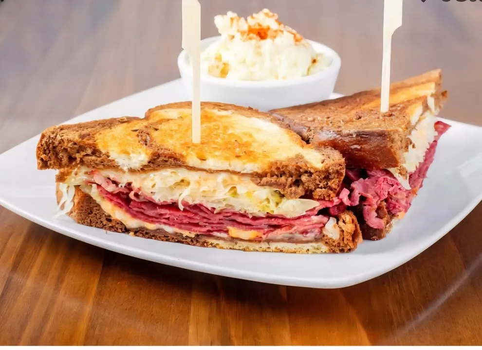 A stacked Reuben on toasted rye, cut to show thick layers of corned beef and sauerkraut, with a side of coleslaw.
