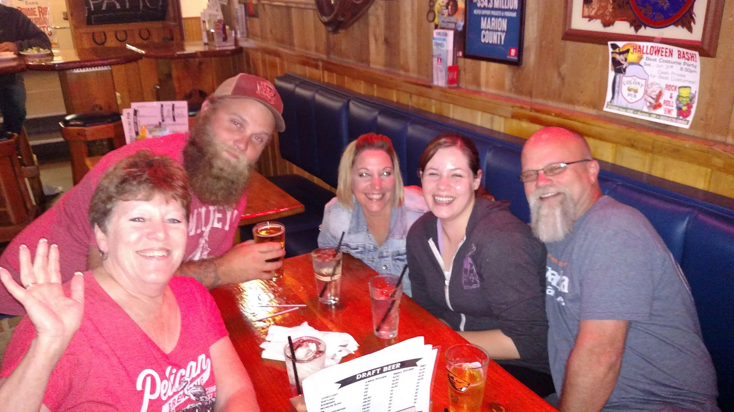 Group of five smiling around a booth, drinks on the table, neon signs lit on the wood walls.