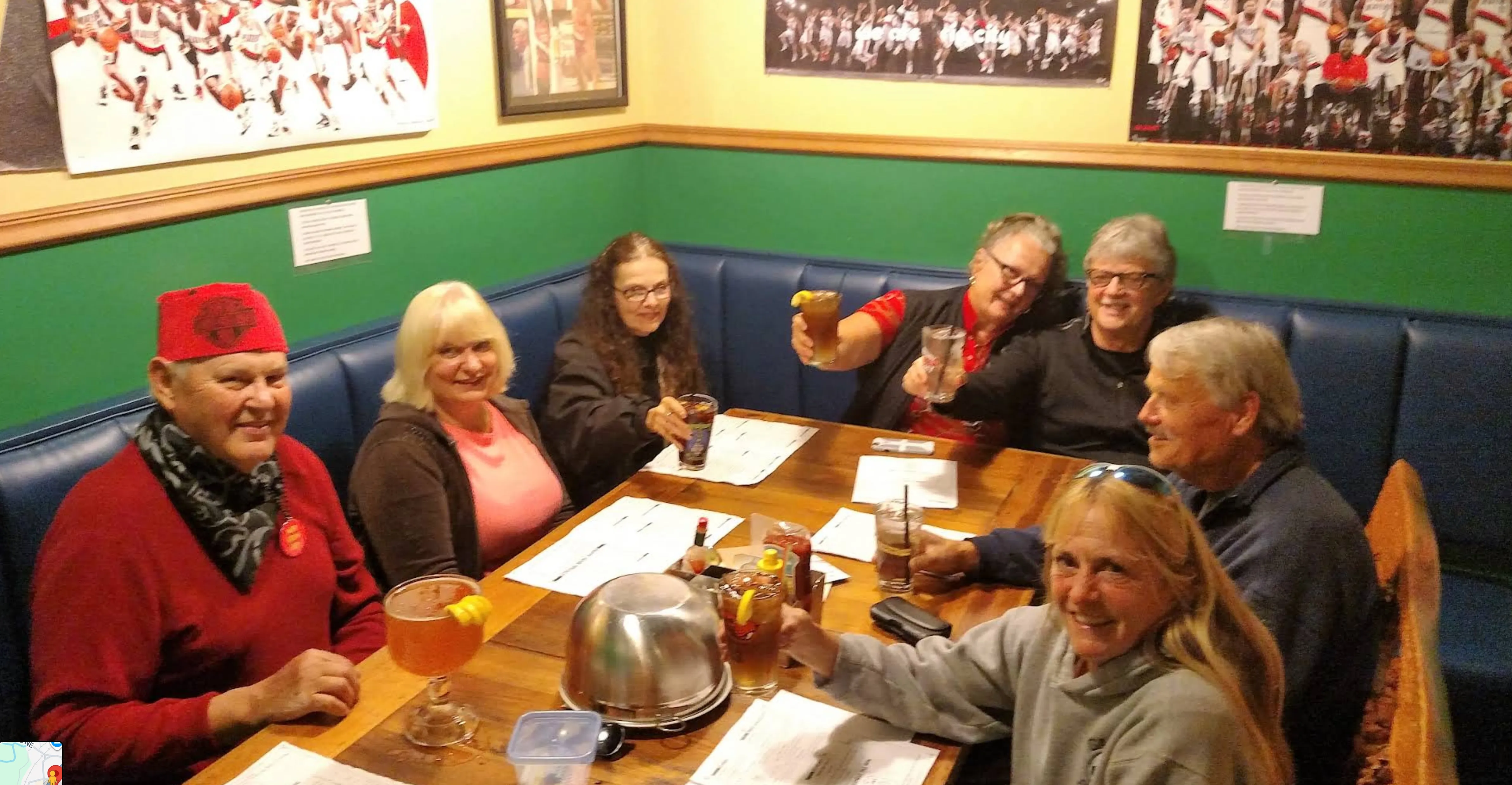 Six friends raising their glasses in a toast around a corner booth.